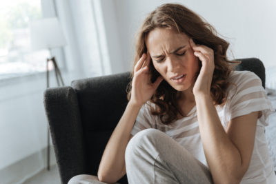 Unbearable headache. Unhappy moody cheerless woman touching her temples and trying to ease the pain while having migraine