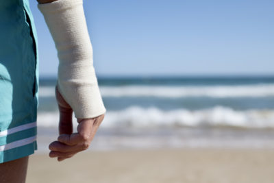 closeup of a young caucasian man in swimsuit on the beach with a bandage in his wrist, in front of the sea, with a negative space on the right