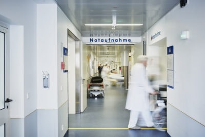Notaufnahme Eingang Krankenhaus mit Arzt Rollstuhl und Patient in Bewegungsunschärfe auf dem Flur