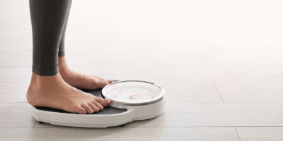 Woman standing on scales indoors, space for text. Overweight problem