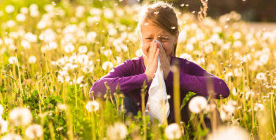 Girl sitting in a meadow with dandelions and has hay fever or allergy