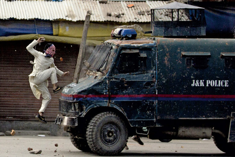 Ein Maskierter bewirft den indischen Polizeiwagen mit Steinen. Hintergrund sind Proteste gegen die Abriegelung des Kaschmirtals.